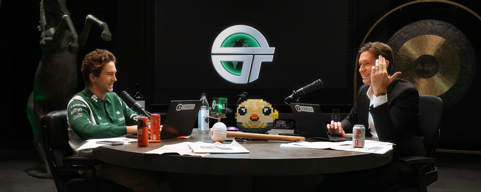 The TBPN studio set — John Coogan and Jordi Hays at the round desk with the TBPN logo and mascot.