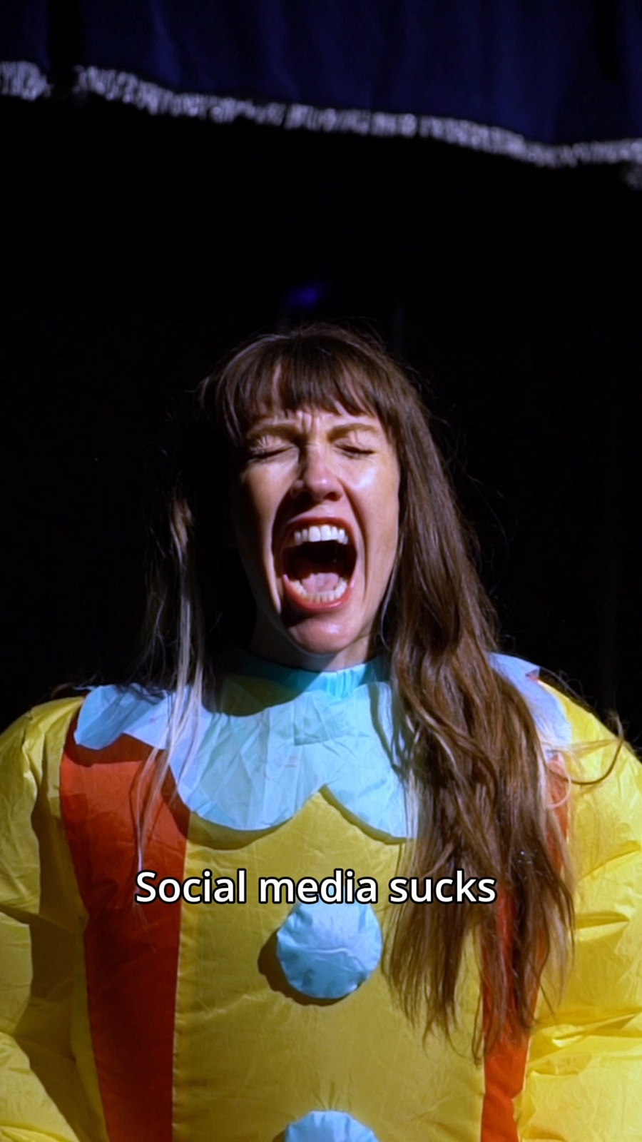 Mieke Marple, self-portrait from the artist's video — wearing an inflatable clown costume, mouth open.